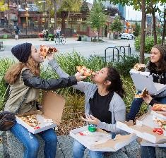 Young people sitting at a parklet eating pizza together